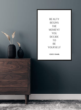 Framed "Beauty begins the moment you decide to be yourself" Coco Chanel quote poster on wall above dresser.