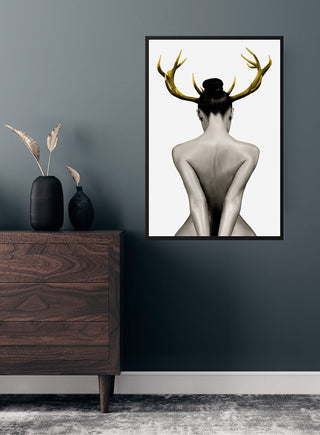 Poster of a naked woman with antlers hanging on a dark wall above a wooden dresser in a modern room.