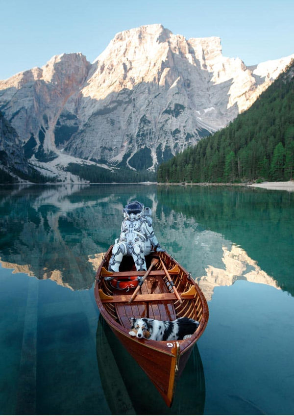 Astronaut sitting in a canoe with two dogs on a calm lake, mountains and forest in the background.
