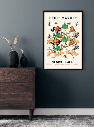 Framed Fruit Market - Venice Beach plakat featuring vibrant butterflies and fruits, hanging on a dark wall.