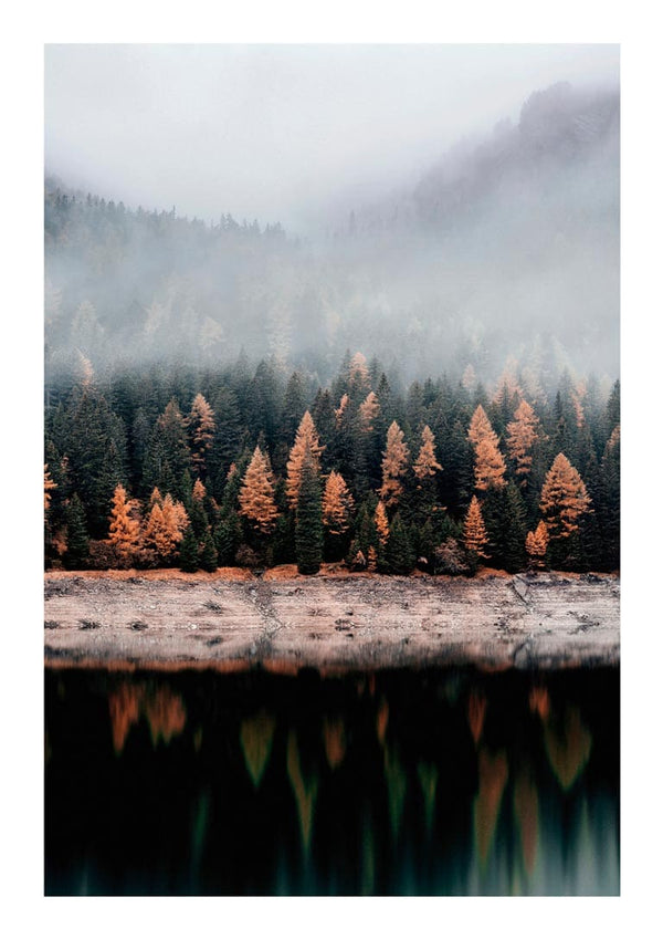 Autumn trees with orange foliage reflected on a calm lake, misty forest and mountains in the background.