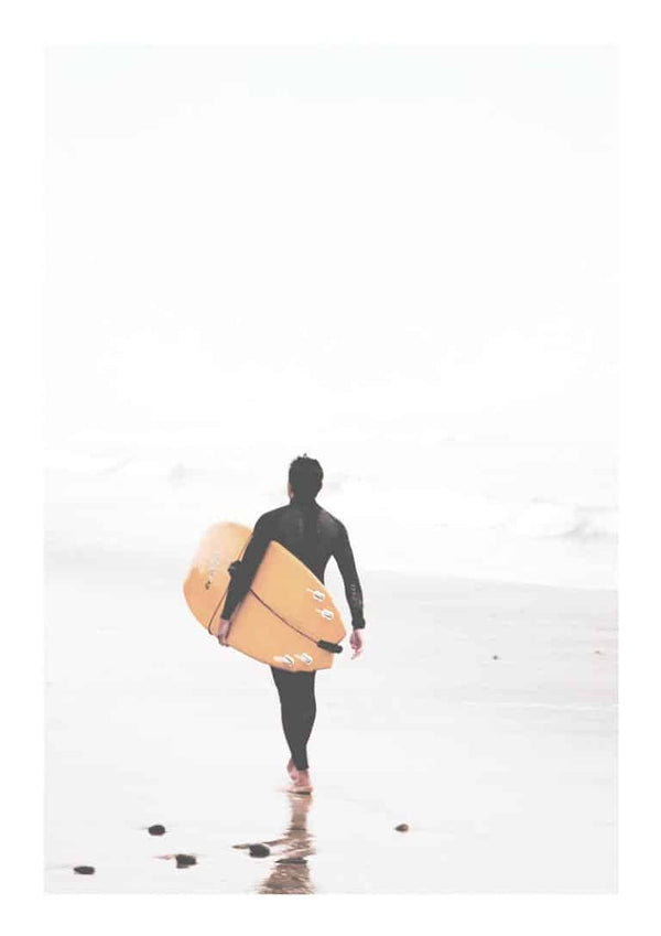 A surfer in a wetsuit walks on the beach carrying a yellow surfboard toward the ocean.