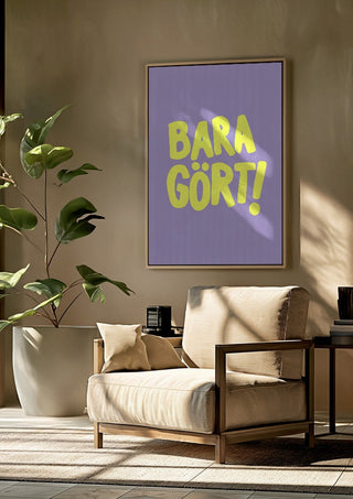 Bara gört! by Grafik bageri framed above a beige armchair beside a potted plant