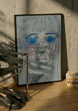Awe by Alice Ruja in a black frame leaning against a concrete wall by a steel chair