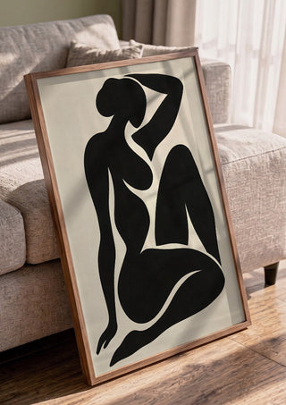 Black Nude Silhouette – Minimalist Abstract Figure Wall Art by TimlessArtworks in a walnut frame leaning against a grey sofa