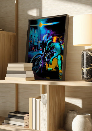 Bike Boys by Pelecan Schneider in a dark frame on a wooden shelf beside books and a lamp