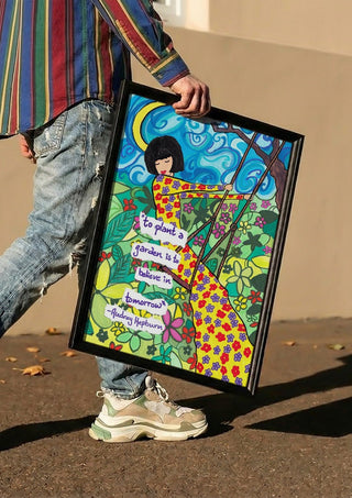 To Plant a Garden by Camilla Nilsson carried in a black frame along a sunny street