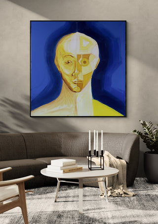 Ochre portrait / blue field by Linor Citaku in a black frame above a curved grey sofa with candlesticks on a round table