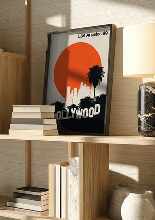 Los Angeles 89 by Bo Lundberg in a dark frame on a wooden shelf beside books and a lamp