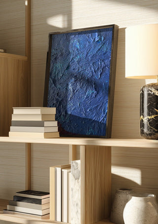 Das Meer by Sophie Schillen in a dark frame on a wooden shelf beside books and a lamp