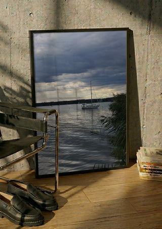 Light Reaching the Water by Bora Kőhalmi in a black frame leaning against a concrete wall by a steel chair