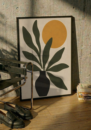Minimalist Botanical Still Life with Sun by TimlessArtworks in a black frame leaning against a concrete wall by a steel chair