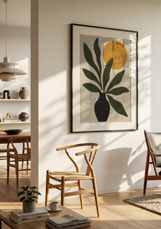 Minimalist Botanical Still Life with Sun by TimlessArtworks in a black frame in a bright dining room with wooden chairs