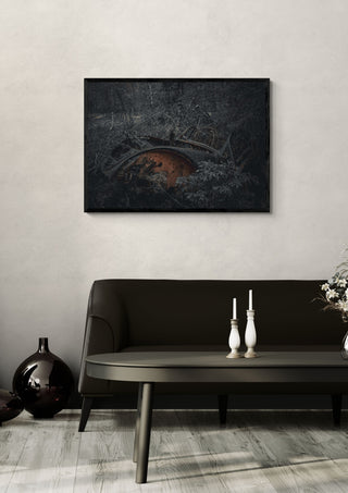 Decay (3) by Lone Gjessing in a black frame on a pale wall above a dark sofa with candlesticks