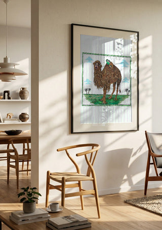 The Camel and the Book by Waldemar Mandzel in a black frame in a bright dining room with wooden chairs