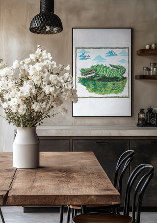 The Crocodile and the Book by Waldemar Mandzel in a black frame above a rustic table with white flowers
