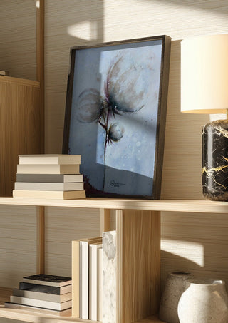 Cotton by Marina Agre in a dark frame on a wooden shelf beside books and a lamp
