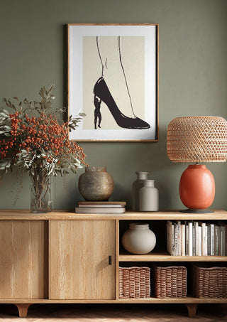 Heavy is the Heel by Nari above a wooden sideboard on a sage green wall