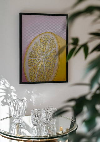 Half Lemon by L.OE. Art in a black frame above a glass table with crystal glassware