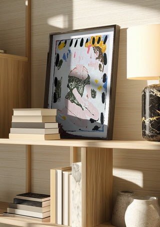 VISA OWNS MY EYES by Oscar Birch in a dark frame on a wooden shelf beside books and a lamp