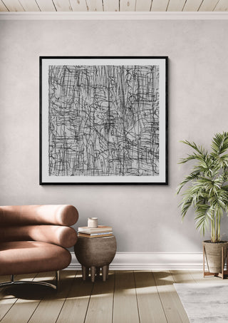 Reel by Priit Ruttas in a black frame above a pink armchair beside a palm