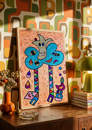 Blue Tree with Faces by Steffi Seiler in a wooden frame on a sideboard against retro patterned wallpaper