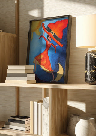 Balance Exercise by A Sleepy Spirit Art in a dark frame on a wooden shelf beside books and a lamp