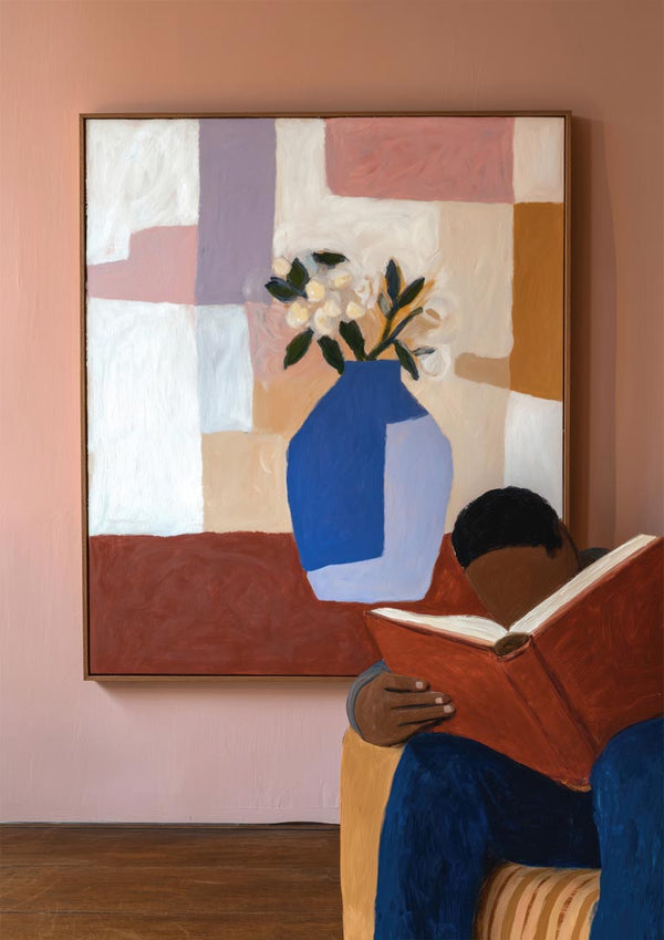 A person reading a large book sits in front of a colorful painting with a blue vase and flowers.