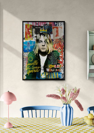 Framed Kurt wall art by Ricardo Noble above a dining table with flowers, lamp, and blue-backed chair.