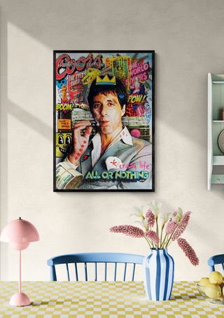 Framed Scarface Vol. 2 - Ricardo Noble artwork hanging on a light wall above a dining table with flowers.