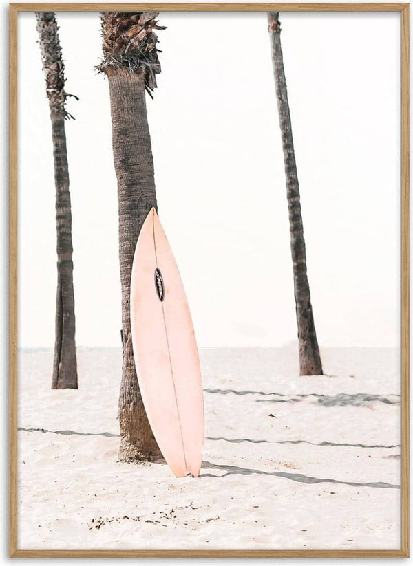A pink surfboard rests against a palm tree on a sandy beach, with clear sky in the background.